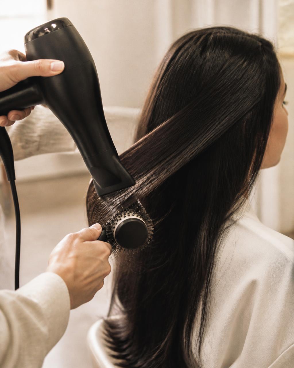 Stylist blow-drying long dark hair with a round brush